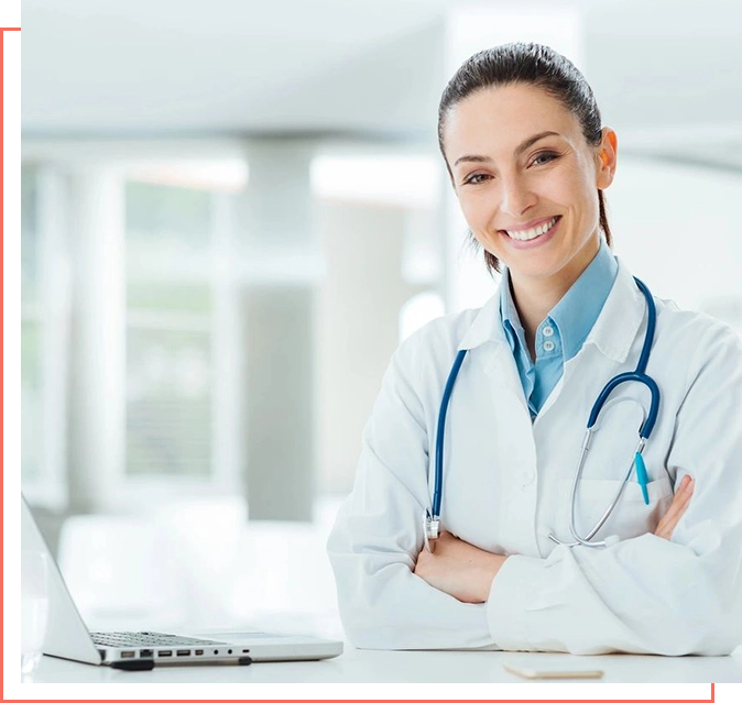 A woman in white lab coat sitting at table with laptop.